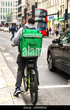 London, England, Vereinigtes Königreich - 28. Juni 2023: Radfahrer, die einen isolierten Container für das Uber-Essenslieferungsunternehmen mit sich führen und an der Ampel warten Stockfoto