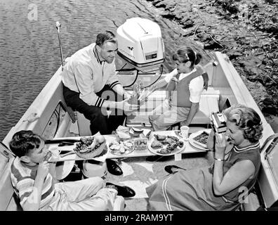 Vereinigte Staaten: c. 1959. Diese Bootsfamilie brauchte einen Tisch für das Mittagessen, also drehten sie die Wasserskier um und legten sie über das Boot für einen Tisch. Stockfoto