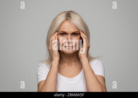 Unglückliche, wunderschöne Seniorin massiert ihre Schläfen, leidet an Kopfschmerzen Stockfoto