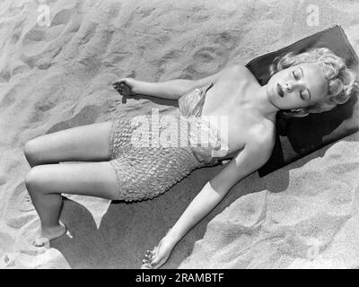 Vereinigte Staaten: c. 1958. Eine hübsche Frau am Strand in einem einteiligen Badeanzug schließt ihre Augen und taucht in die Sonnenstrahlen ein. Stockfoto