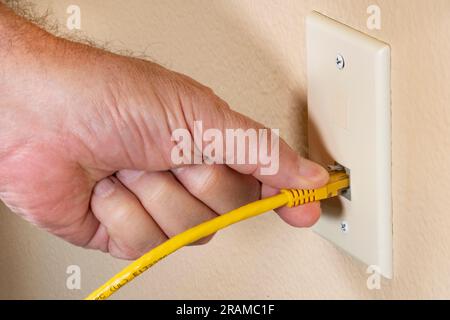 Man steckt das gelbe ethernet-Kabel RJ45 mit der Hand in die Heimnetzwerkbuchse Stockfoto