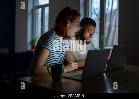 Glückliches, vielseitiges Paar hat kleine Online-Geschäfte zu Hause und arbeitet abends mit Laptops Stockfoto