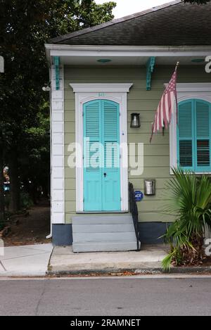 Malerisches einstöckiges grünes kreolisches Cottage mit weißen Zierleisten und blauen Fensterläden im historischen Viertel Faubourg Marigny, New Orleans. Stockfoto