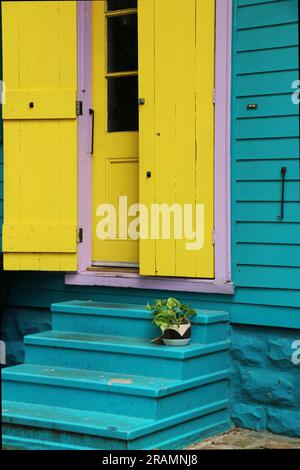 Leuchtend gelbe Fensterläden umrahmen eine gelbe Tür in einem blauen kreolischen Cottage im Faubourg Marigny District, New Orleans. Stockfoto