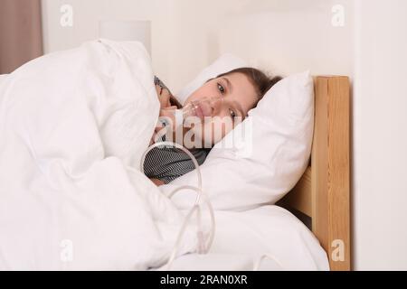 Süßes Mädchen, das zu Hause einen Vernebler zur Inhalation am Bett benutzt Stockfoto