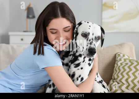 Eine schöne Frau, die ihren niedlichen dalmatinischen Hund zu Hause auf dem Sofa umarmt. Hübsches Haustier Stockfoto