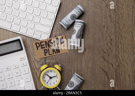 Karte mit Wörtern Pensionsplan, Banknoten, Taschenrechner und Wecker auf hölzernem Bürotisch, flach liegend. Platz für Text Stockfoto
