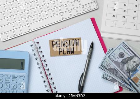 Karte mit Worten Pensionsplan, Banknoten, Taschenrechner und Notizbuch auf weißem Bürotisch, flach liegend Stockfoto