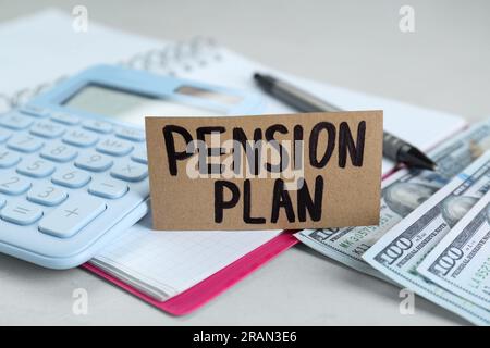 Karte mit Worten Pensionsplan, Banknoten, Taschenrechner und Notizbuch auf weißem Tisch, Nahaufnahme Stockfoto