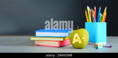 Apfel mit geschnitztem Buchstaben A und Pluszeichen als Sorte. Schulpapier auf weißem Tisch im Klassenzimmer. Bannerdesign mit Platz für Text Stockfoto