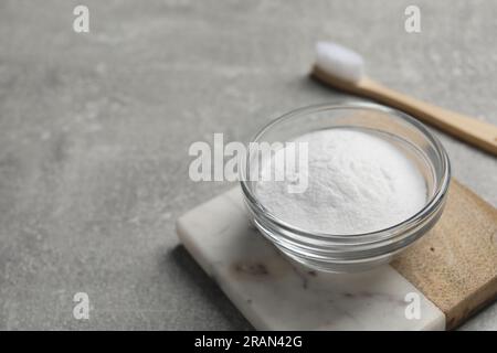 Bambuszahnbürste und Schüssel mit Backpulver auf grauem Tisch, Nahaufnahme. Platz für Text Stockfoto