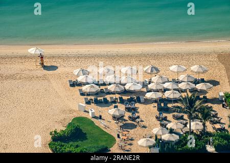 Strand mit Touristen, die die Sonne und das Meer genießen, sitzen unter Sonnenschirmen aus der Vogelperspektive von oben. Stockfoto