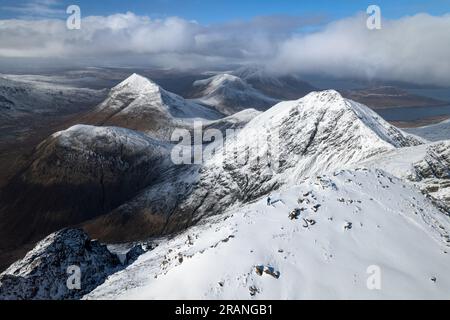 Luftaufnahme eines Mannes, der auf dem schneebedeckten Bla Bheinn-Berg steht und die schneebedeckte Landschaft der Isle of Skye, Schottland, bestaunt Stockfoto