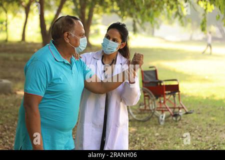 Ärztin, die sich um Seniorpatienten im Krankenhausgarten kümmert. Der Patient ist gehbehindert und wird von einem spezialisierten Hausarzt behandelt Stockfoto