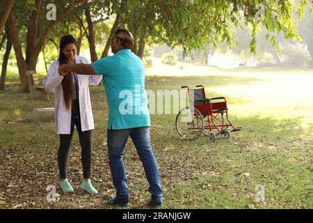 Weibliche indische Ärztin kümmert sich um Seniorpatienten im Krankenhausgarten. Der Patient ist gehunfähig Stockfoto