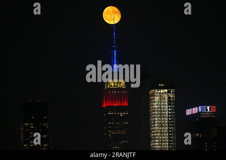 New York City, Usa. 04/07/2023, Vollmond erhebt sich hinter dem Empire State Building, das zu Ehren des Unabhängigkeitstages am 4. Juli in New York City, USA, in den Farben der amerikanischen Flagge erleuchtet ist. Kredit: Brasilien Photo Press/Alamy Live News Stockfoto