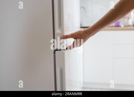 Weibliche Hand öffnet weiße Kühlschranktür Stockfoto