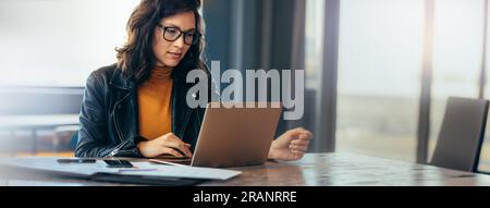 Asiatische Geschäftsfrau sitzt an einem Tisch in einem Büro und tippt mit Fokus auf ihrem Laptop. Junge weibliche Fachkraft zeigt Hingabe und Hingabe Stockfoto