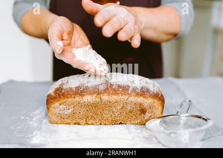 Weibliche Bäckerhände halten gebackenes hausgemachtes Mehlbrot Stockfoto