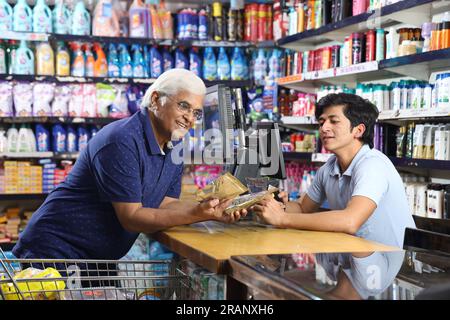 Großvater kaufte im Supermarkt ein und stand auf der Rechnung. Der alte Großvater mit weißem Haar zeigt sein gewünschtes Verbrauchsmaterial und passt zu den Preisen. Stockfoto