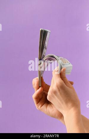Weibliche Hände halten einen Stapel amerikanischer Dollar auf lila Hintergrund. Banknoten von 100 Dollar in Händen. Das Konzept des Geschäfts, des Finanzwesens Stockfoto
