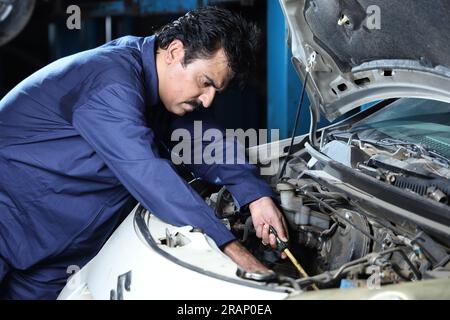 Schnurrbartmechaniker bei der Reparatur und Untersuchung des Autos. Ein Autospezialist verwendet Reparaturwerkzeuge. Ein Mechaniker in blauer Mechanikeruniform. Stockfoto