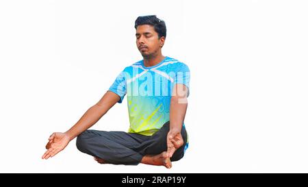 Junger indischer Mann in sportlichen Outfits, der Yoga macht und vor weißem Hintergrund meditiert Stockfoto