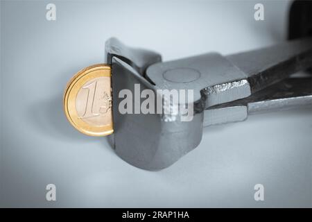Eine Zange, die in eine Euro-Münze beißt, das Konzept der wirtschaftlichen Inflation, die die Kaufkraft verringert. Stockfoto