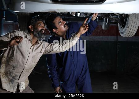 Mechaniker stehen und arbeiten in der Servicestation zusammen. Autospezialisten untersuchen das angehobene Auto. Professionelle Handwerker, die reden, auftreten. Stockfoto