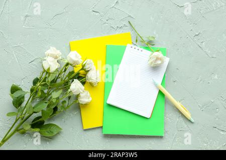Verschiedene Notizbücher, Stifte und wunderschöne Rosenblumen auf Grunge-Hintergrund Stockfoto