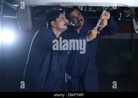 Mechaniker stehen und arbeiten in der Servicestation zusammen. Autospezialisten untersuchen das angehobene Auto. Professionelle Handwerker, die reden, auftreten. Stockfoto