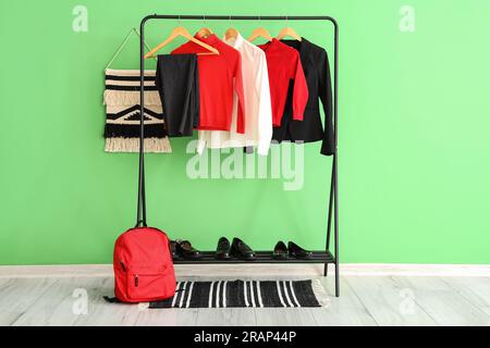 Stilvolle Schuluniform, die an einem Regal, einem Rucksack und Schuhen in der Nähe der grünen Wand im Zimmer hängt Stockfoto