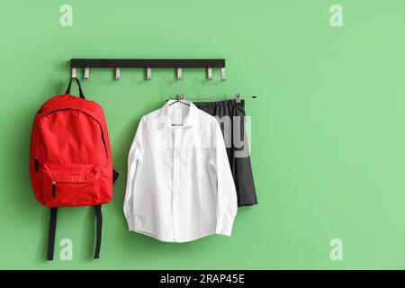 Stilvolle Schuluniform und Rucksack, die an der grünen Wand des Zimmers hängen Stockfoto