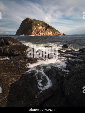 Wasser floss auf Felsen in der Nähe einer großen Insel im Meer Stockfoto