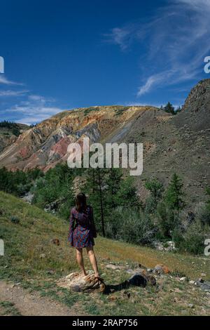 Eine junge Frau in einem kurzen Kleid steht vor der Kulisse des berühmten Wahrzeichens Altai Mars im Canyon. Sommerreisekonzept Stockfoto