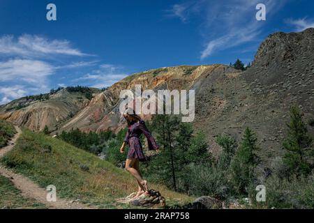 Eine junge Frau in einem kurzen Kleid steht neben einem Wanderweg vor der Kulisse des berühmten Wahrzeichens Altai Mars im Canyon. Sommerurlaub CONT Stockfoto