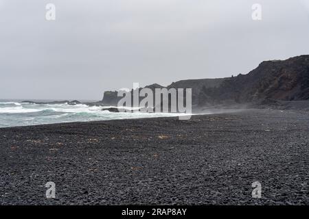 Wellen waschten sich gegen den schwarzen Sandstrand von Djupalonssandur in Island Stockfoto