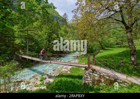 Frau überquert den Fluss Soca mit ihrem elektrischen Mountainbike über eine Hängebrücke im Triglav-Nationalpark in Slowenien Stockfoto