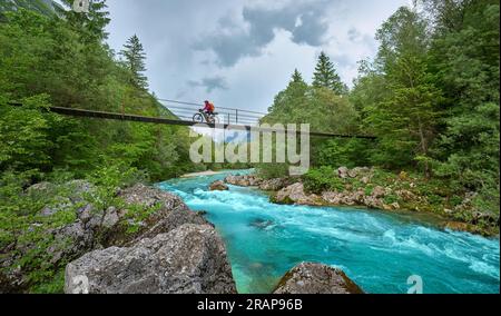 Frau überquert den Fluss Soca mit ihrem elektrischen Mountainbike über eine Hängebrücke im Triglav-Nationalpark in Slowenien Stockfoto