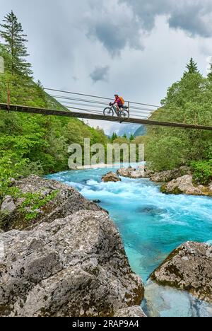 Frau überquert den Fluss Soca mit ihrem elektrischen Mountainbike über eine Hängebrücke im Triglav-Nationalpark in Slowenien Stockfoto