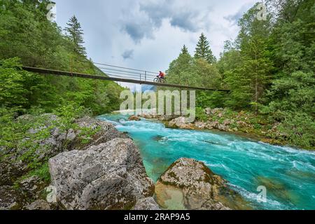 Frau überquert den Fluss Soca mit ihrem elektrischen Mountainbike über eine Hängebrücke im Triglav-Nationalpark in Slowenien Stockfoto