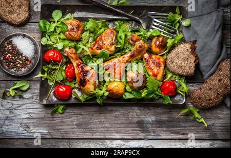 Würzig gebratene Hähnchenschenkel mit Kartoffeln und Salat. Draufsicht. Essen im rustikalen Stil. Stockfoto