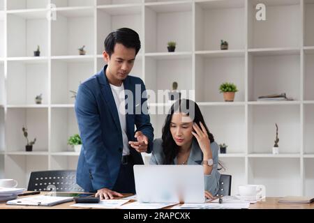 Zwei Geschäftsleute, die während der Arbeit an einem Notebook in einem Büro gestresst sind, Geschäftspartner arbeiten zusammen und analysieren die Teamarbeit Stockfoto
