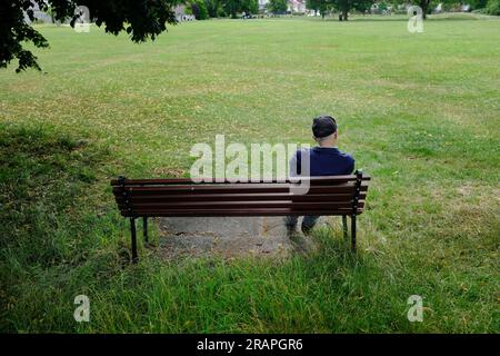 Ein alter Mann, der auf einer Parkbank sitzt. Stockfoto