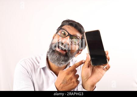 Mittelalter, bärtiger Indianer, der ein Hemd in der Hand hält und ein Handy in der Hand zeigt. Flippige Ausdrücke auf einem Ebenen Hintergrund. Stockfoto