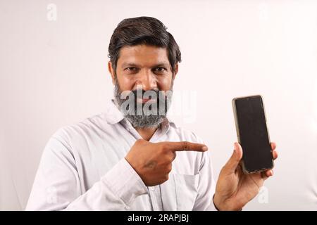 Mittelalter, bärtiger Indianer, der ein Hemd in der Hand hält und ein Handy in der Hand zeigt. Flippige Ausdrücke auf einem Ebenen Hintergrund. Stockfoto