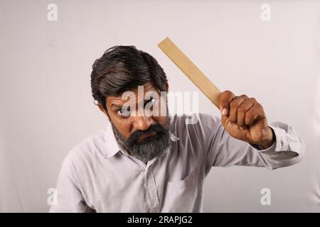 Porträt eines bärtigen Indianers, der im Zorn ein Hemd trägt und ein Lineal in der Hand hält. Seltsame Ausdrücke eines Psycholehrers. Betäubt öffnete sich wütende Augen. Stockfoto