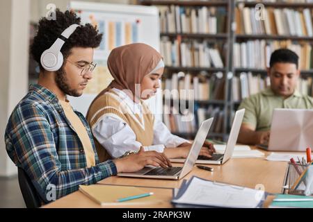 Gruppe ausländischer Studenten, die Computer in ihrem Studium benutzen, während sie in der Bibliothek an einem Tisch sitzen Stockfoto