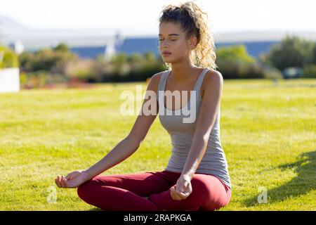 Birassische Frau, die auf dem Gras sitzt, Yoga macht und im Garten meditiert. Sport, gesunder und aktiver Lebensstil, Sommer, Sonnenschein, unverfälscht. Stockfoto