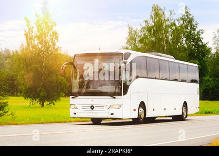 Weißer Mercedes-Benz Tourismo-Bus mit hoher Geschwindigkeit auf der Straße im goldenen Sonnenlicht des Sommers. Salo, Finnland. 22. Juni 2023. Stockfoto